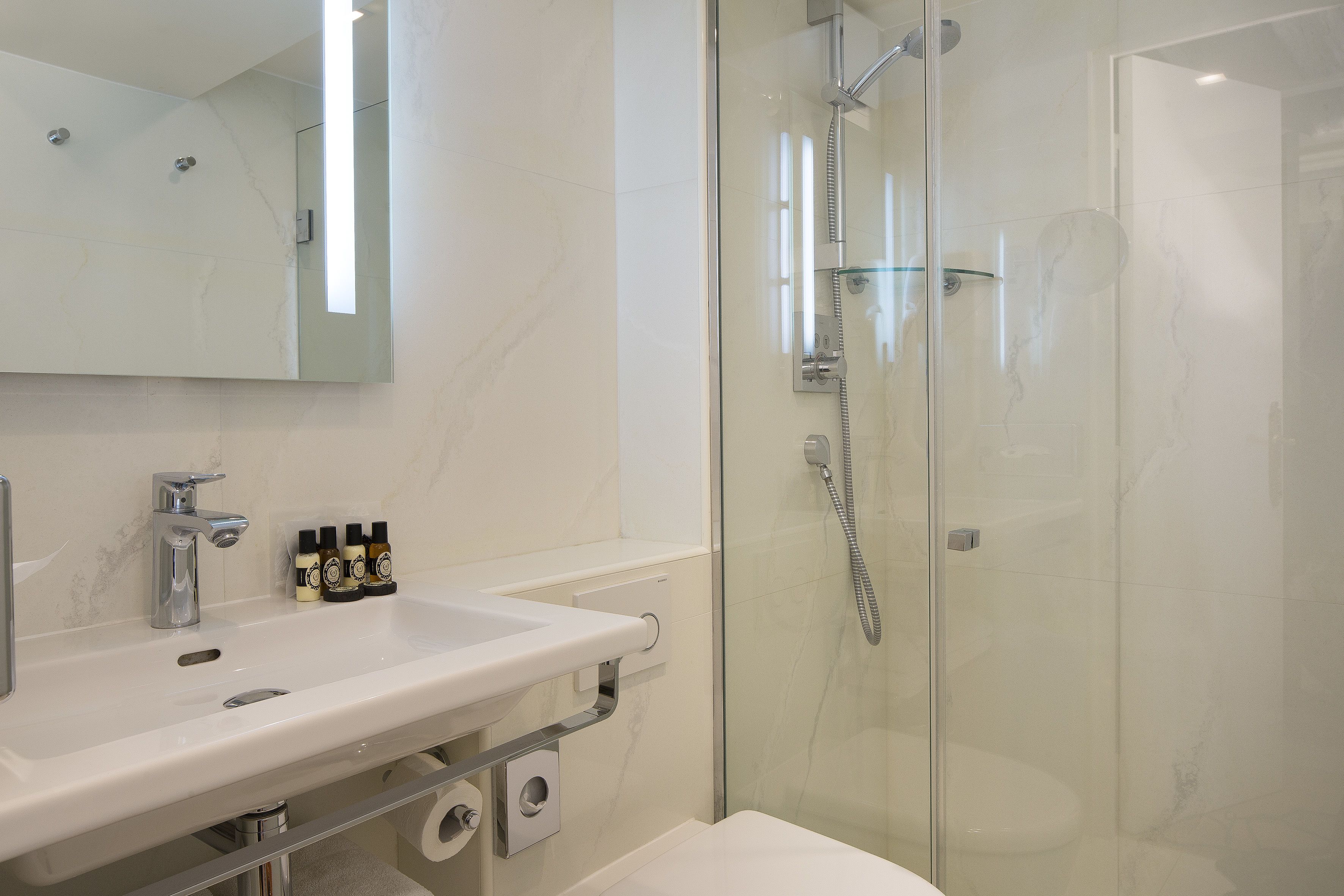 A modern bathroom with a glass-enclosed shower, a white sink with a mirror above, and toiletries on the sink.