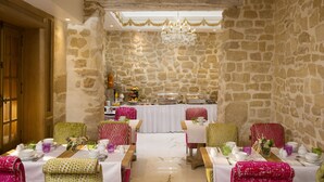 A dining area with stone walls, wooden ceiling beams, and a chandelier. Tables are set with white tablecloths and colorful chairs. - Académie Hôtel Saint Germain (Paris)