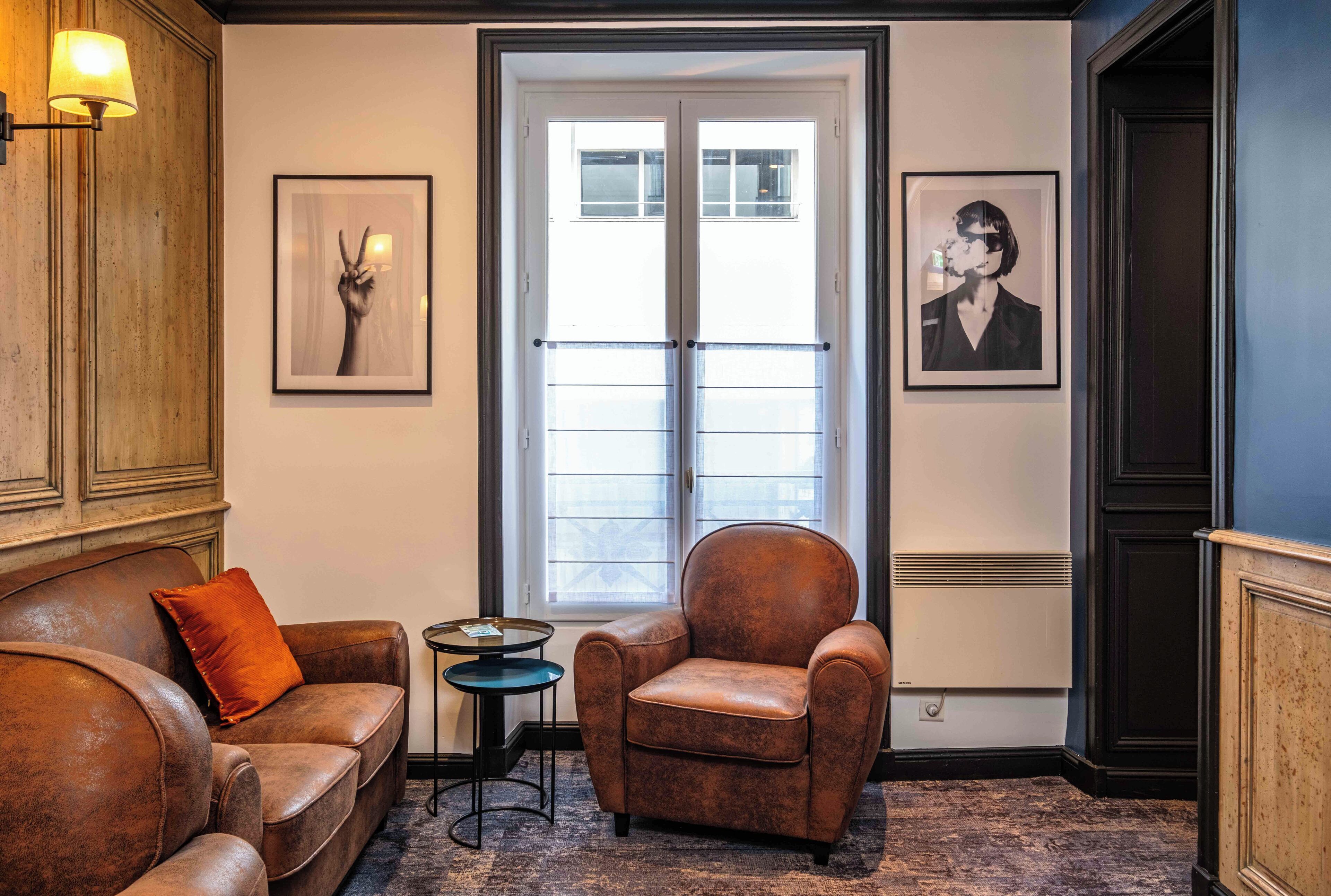 Una habitación con un sofá de cuero marrón, un sillón de cuero marrón, una mesita redonda y dos cuadros en las paredes.