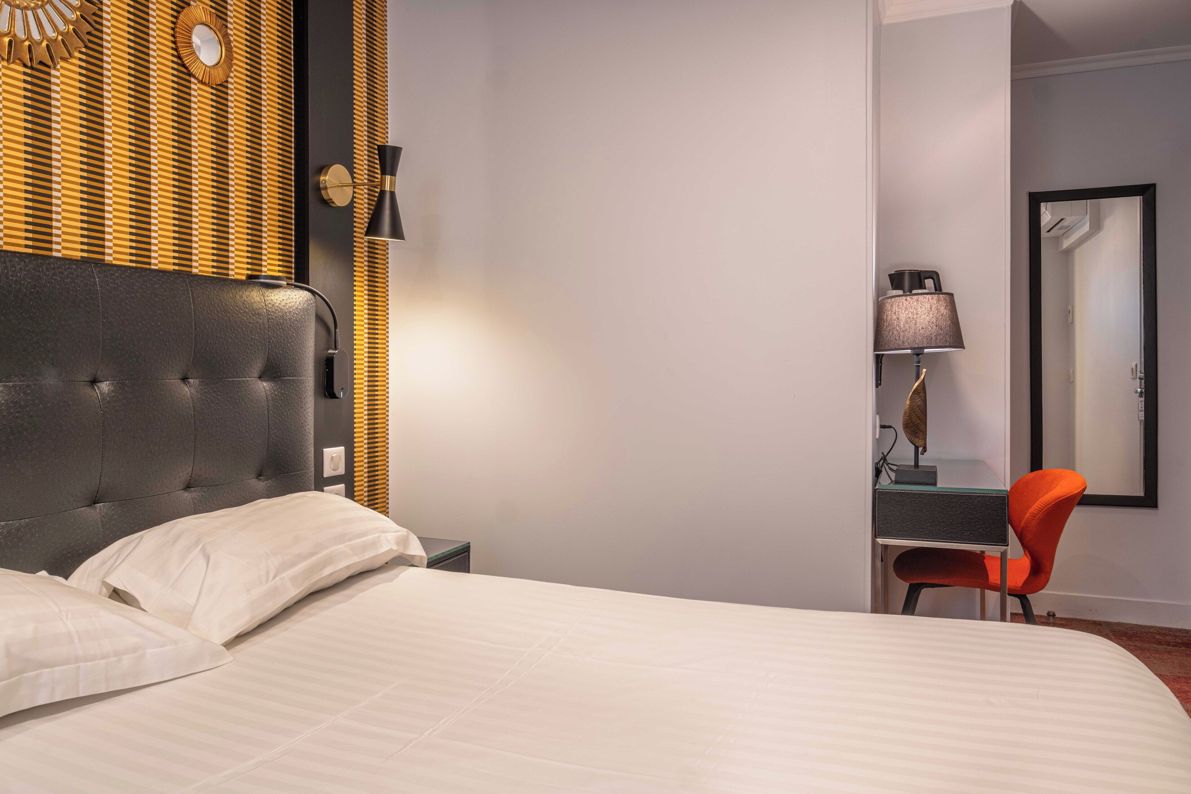 Quarto de hotel com uma cama grande, uma escrivaninha com cadeira, uma luminária e um espelho.