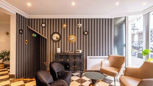 Een hal met een geruit vloerkleed, zwarte en gouden decoratie en twee leren fauteuils.