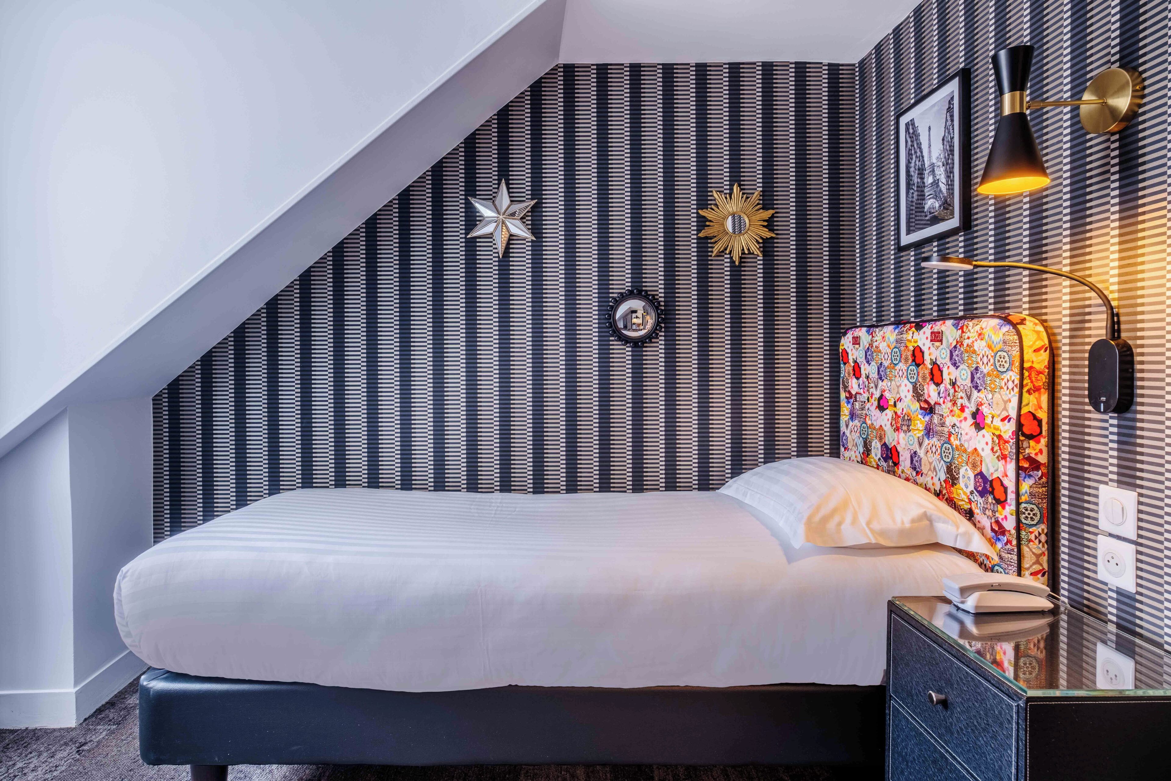 A modern bedroom with a striped wallpaper, a star-shaped decoration, a colorful headboard, and a bedside lamp.