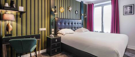 A hotel room with a large bed, a desk with a chair, a nightstand, and a window with curtains.