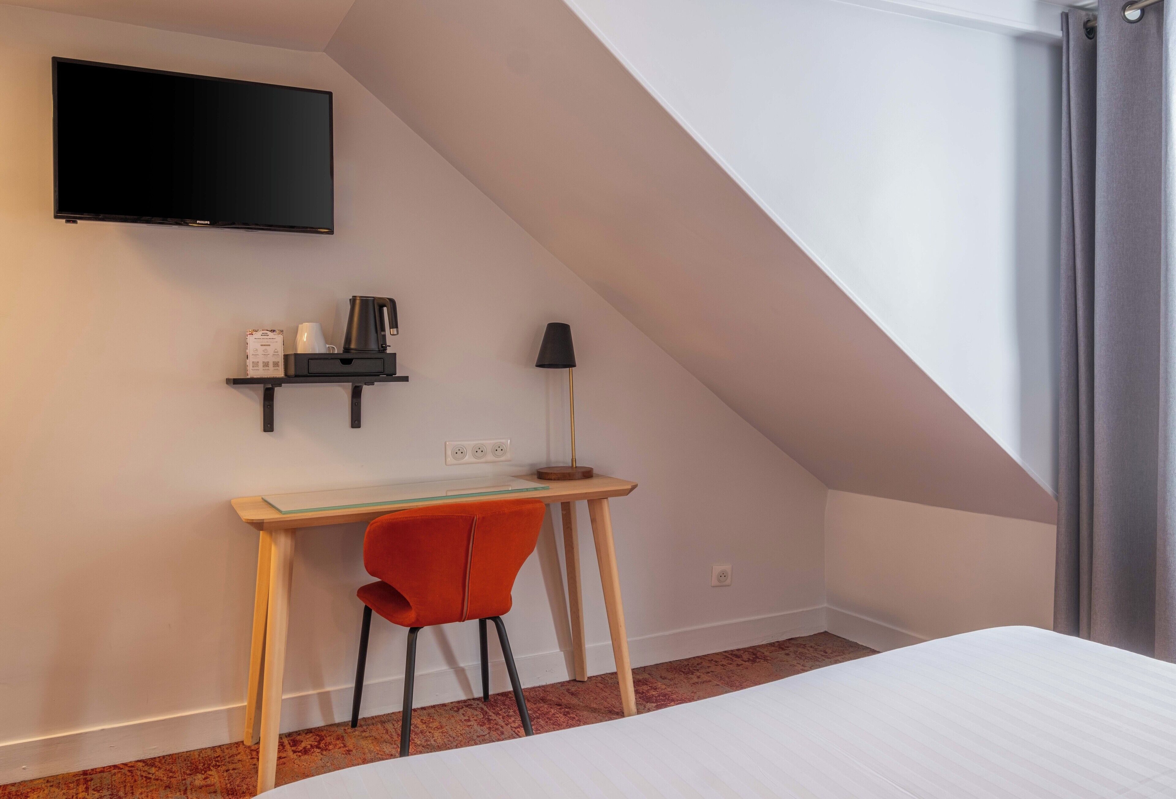 Habitación con cama, un escritorio y silla, televisor montado en la pared y ventana con cortinas.