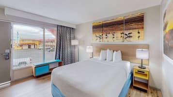 Un cuarto de hotel con una cama grande, vista de la ciudad a través de una puerta corrediza, un banco junto a la ventana y obras de arte en las paredes.