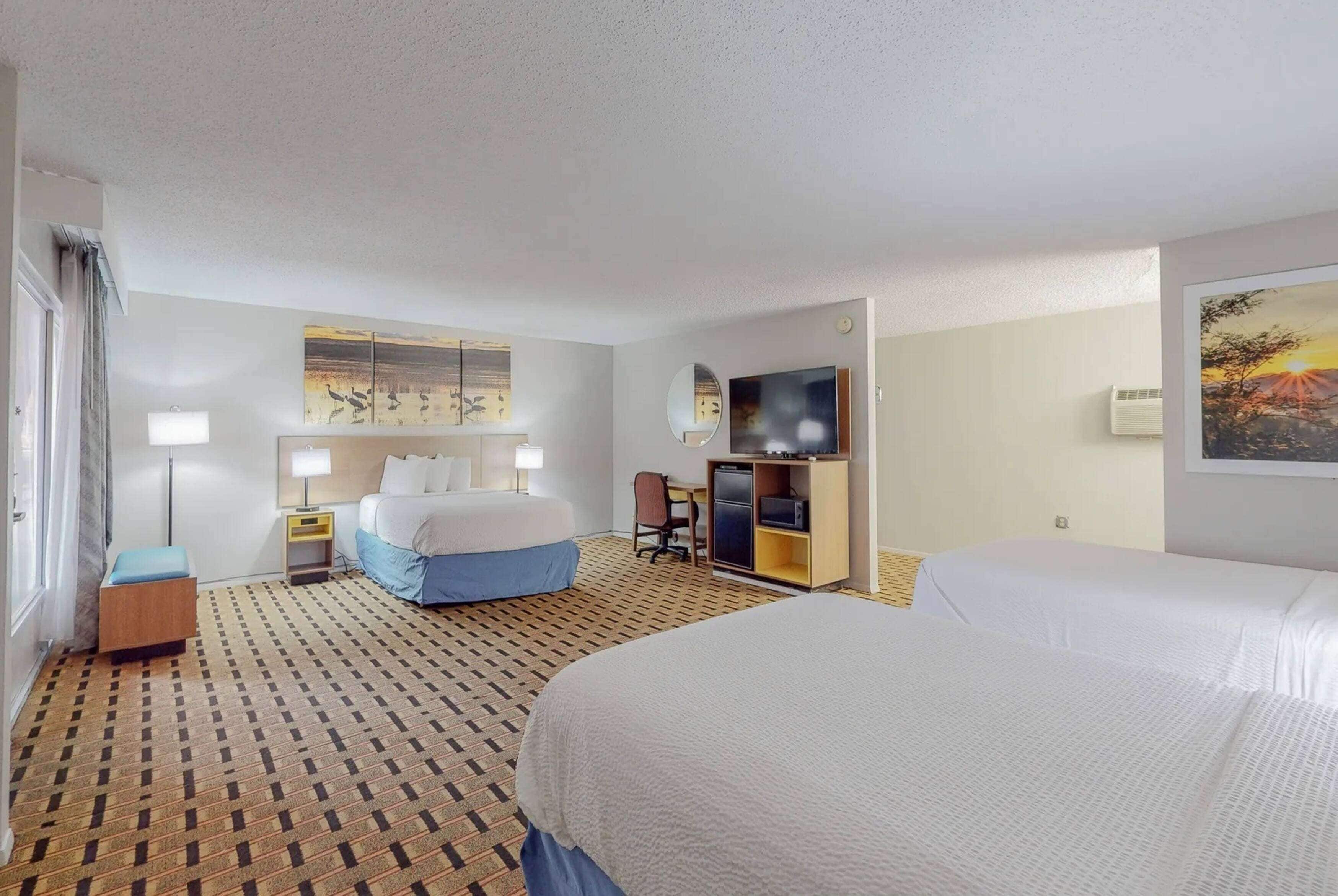 A hotel room with two beds, a desk, a chair, a TV, and artwork on the walls.