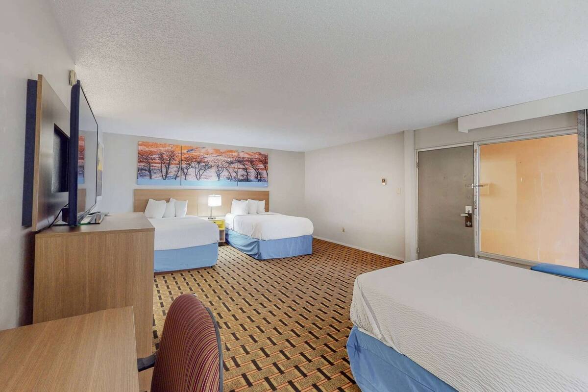 Quarto de hotel com duas camas, uma escrivaninha, uma televisão e um quadro na parede.