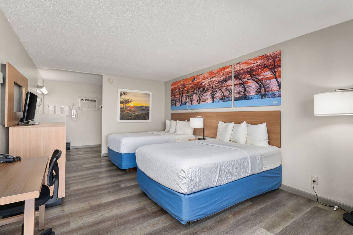 Quarto de hotel com duas camas, uma escrivaninha, uma cadeira, uma televisão e obras de arte na parede.