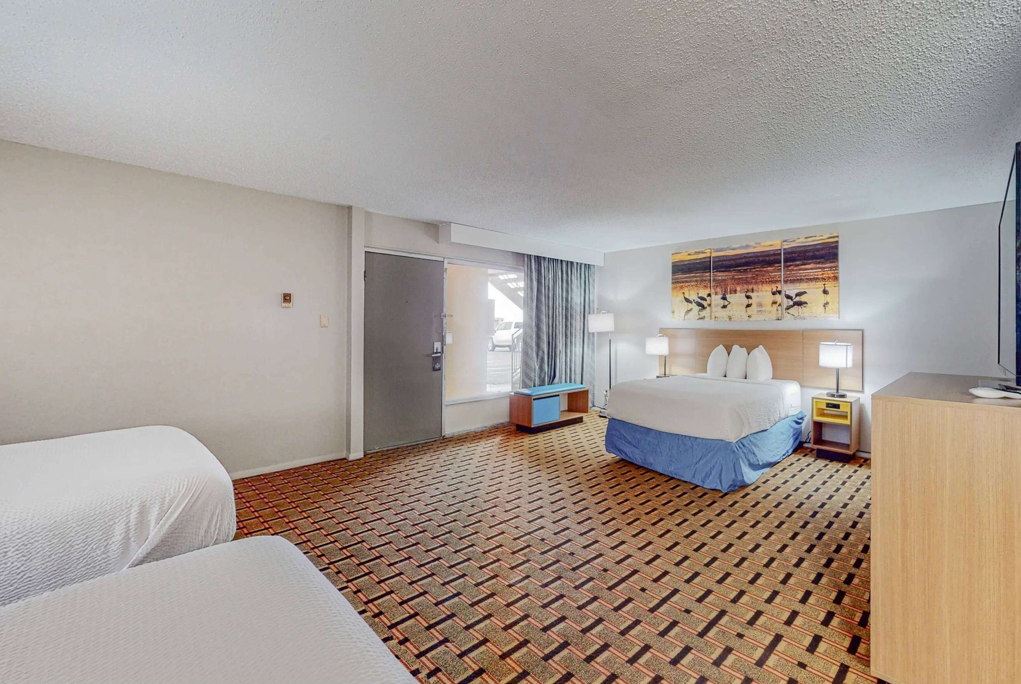 A hotel room with a bed, two bedside tables, a desk, and a patterned carpet.