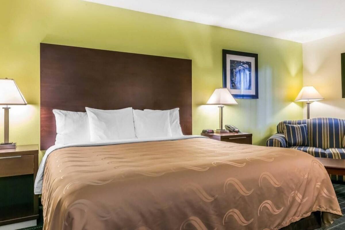 A hotel room with a large bed, two bedside tables, a chair, and a framed picture on the wall.
