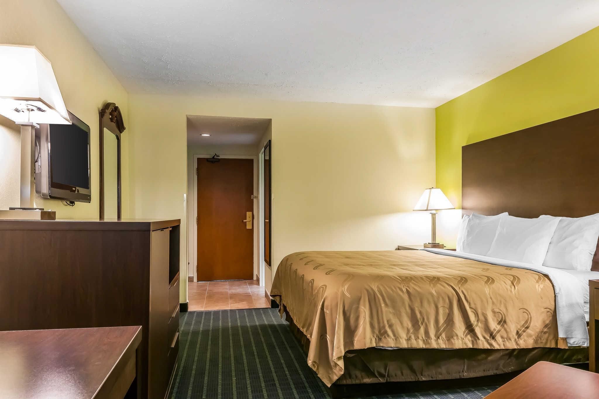 Une chambre d’hôtel comprenant un lit, un bureau, une télévision, une lampe et une porte donnant sur une autre pièce.