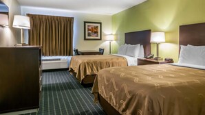 A hotel room with two beds, a desk, a chair, a lamp, a phone, and a picture on the wall.