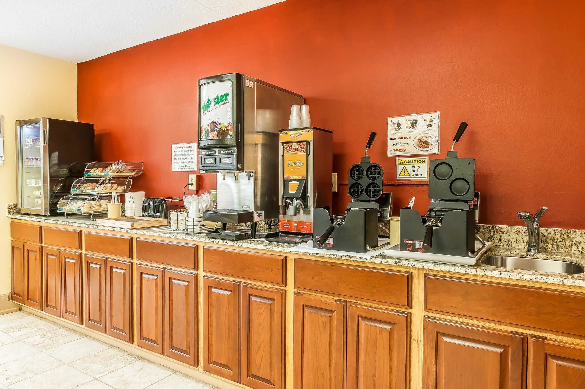 A self-service coffee station with multiple coffee machines, a waffle maker, and a display case with pastries.