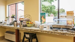 A breakfast bar with a coffee machine, fruit bowl, and a sign indicating a healthy option.