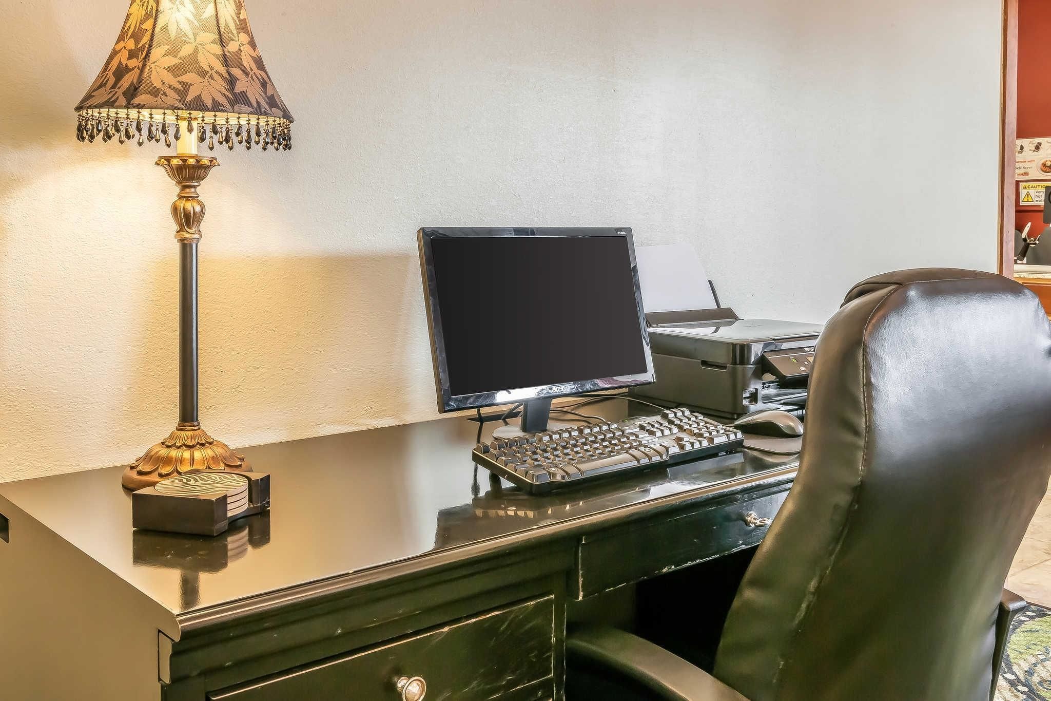 Habitación de hotel con escritorio, ordenador, teclado, lámpara y sillón de cuero.