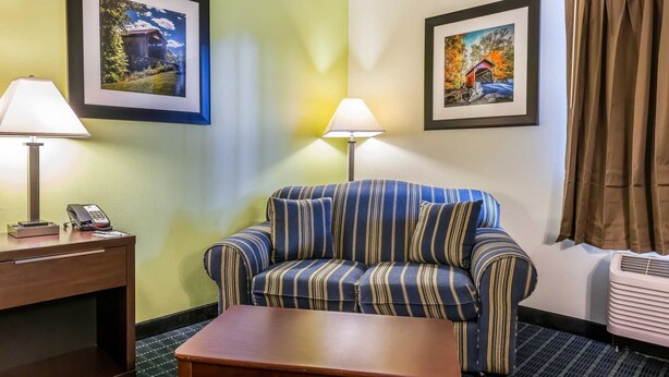 A hotel room with a striped sofa, two wall-mounted lamps, a desk with a phone, and framed pictures on the walls.