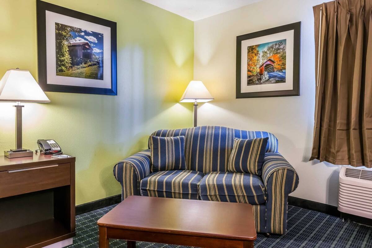 A hotel room with a striped sofa, two wall-mounted lamps, a desk with a phone, and framed pictures on the walls.