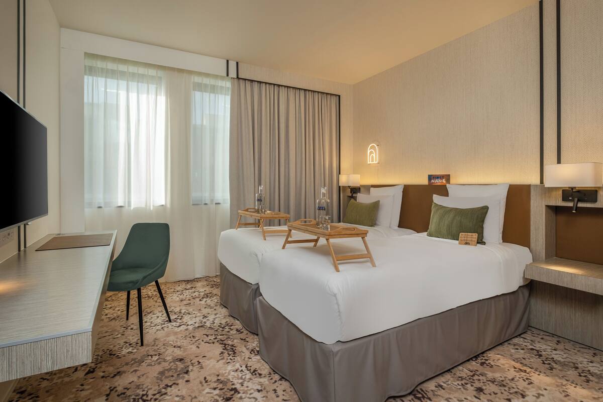 A hotel room with a large bed, a desk with a chair, a TV, and a window with curtains.