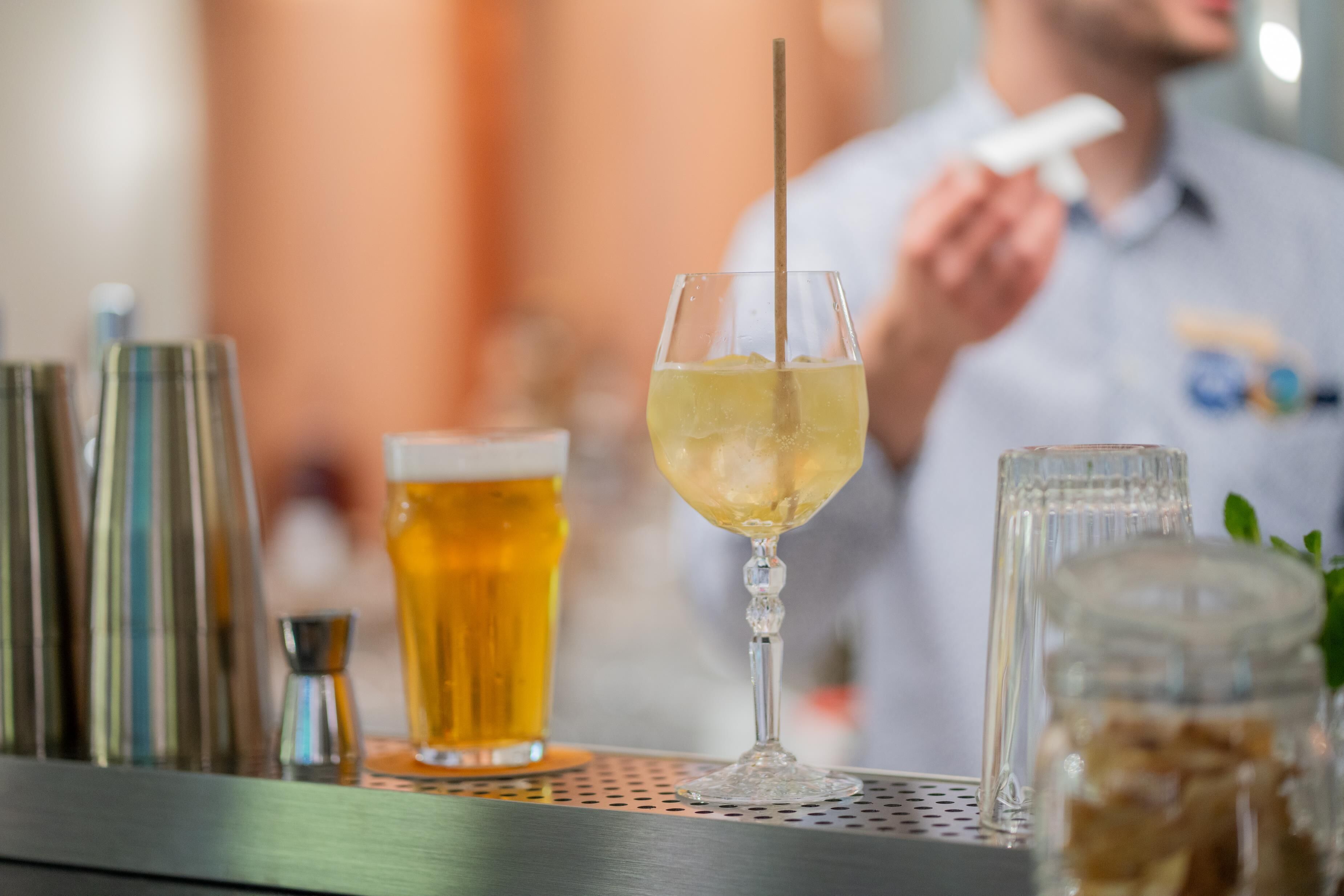 En bardisk med ett glas öl och en cocktail, en bartender och barutrustning.