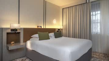 A hotel room with a large bed, two bedside tables with lamps, a small shelf with a lamp, and a window with curtains.
