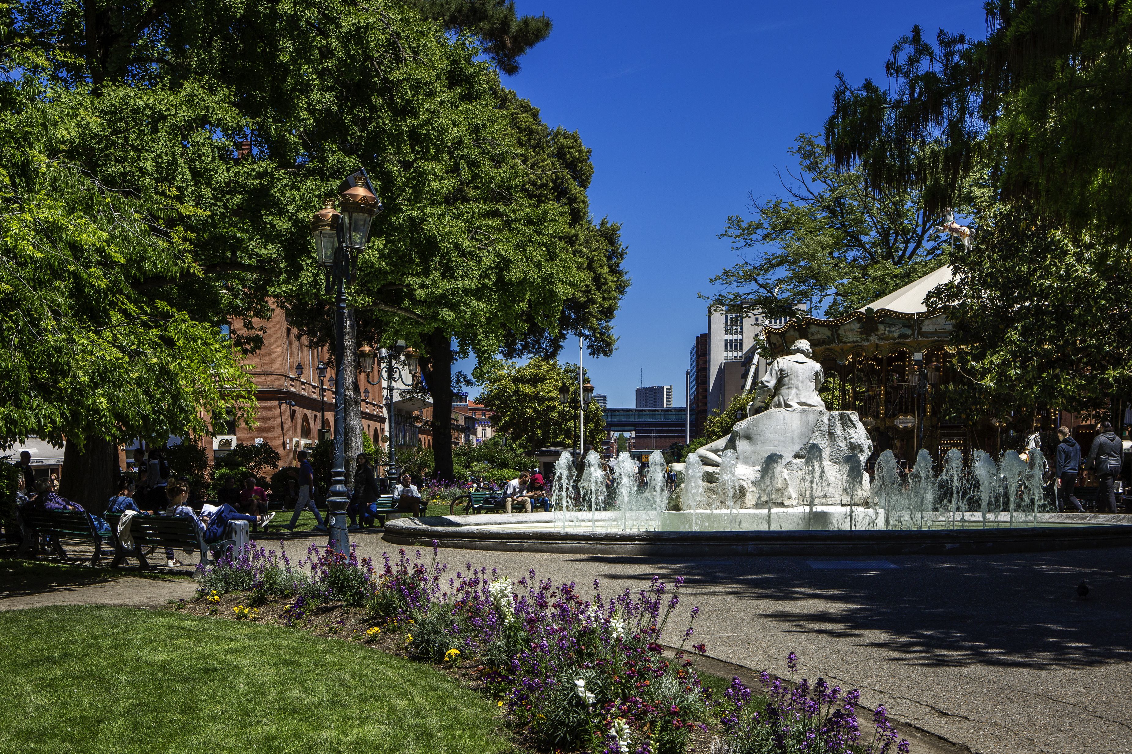 A public square with a fountain, benches, and a statue.