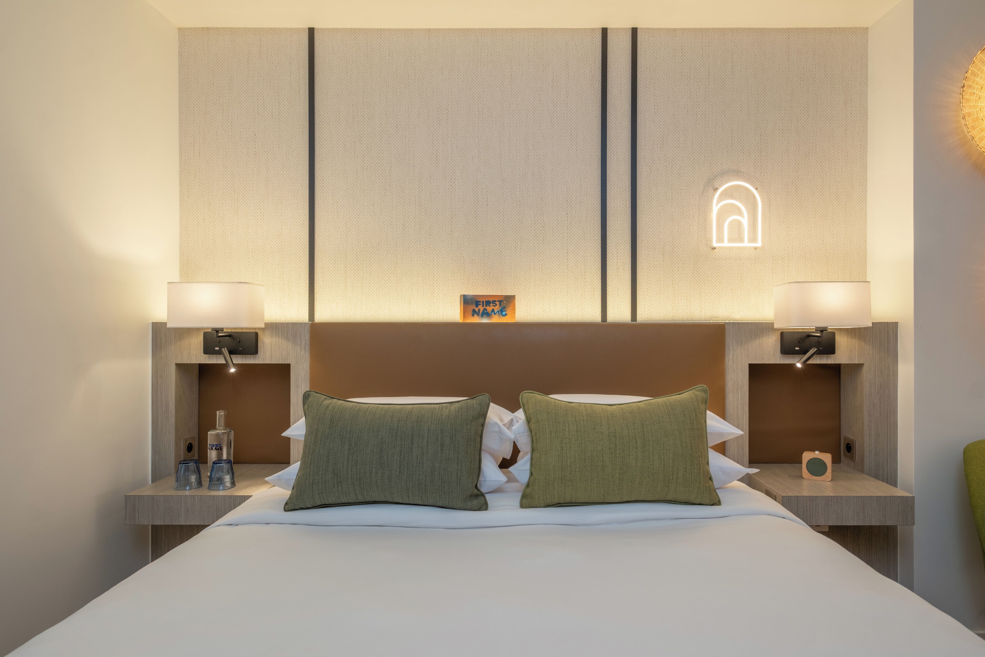 Ein Hotelzimmer mit einem großen Bett, zwei Nachttischen, einer Wandleuchte und einem kleinen dekorativen Gegenstand am Kopfteil.