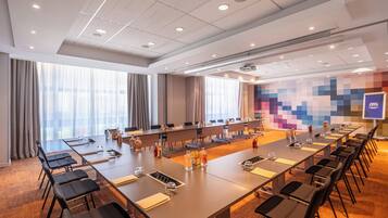 Une salle de conférence équipée de longues tables, de chaises et d’un écran de projection.