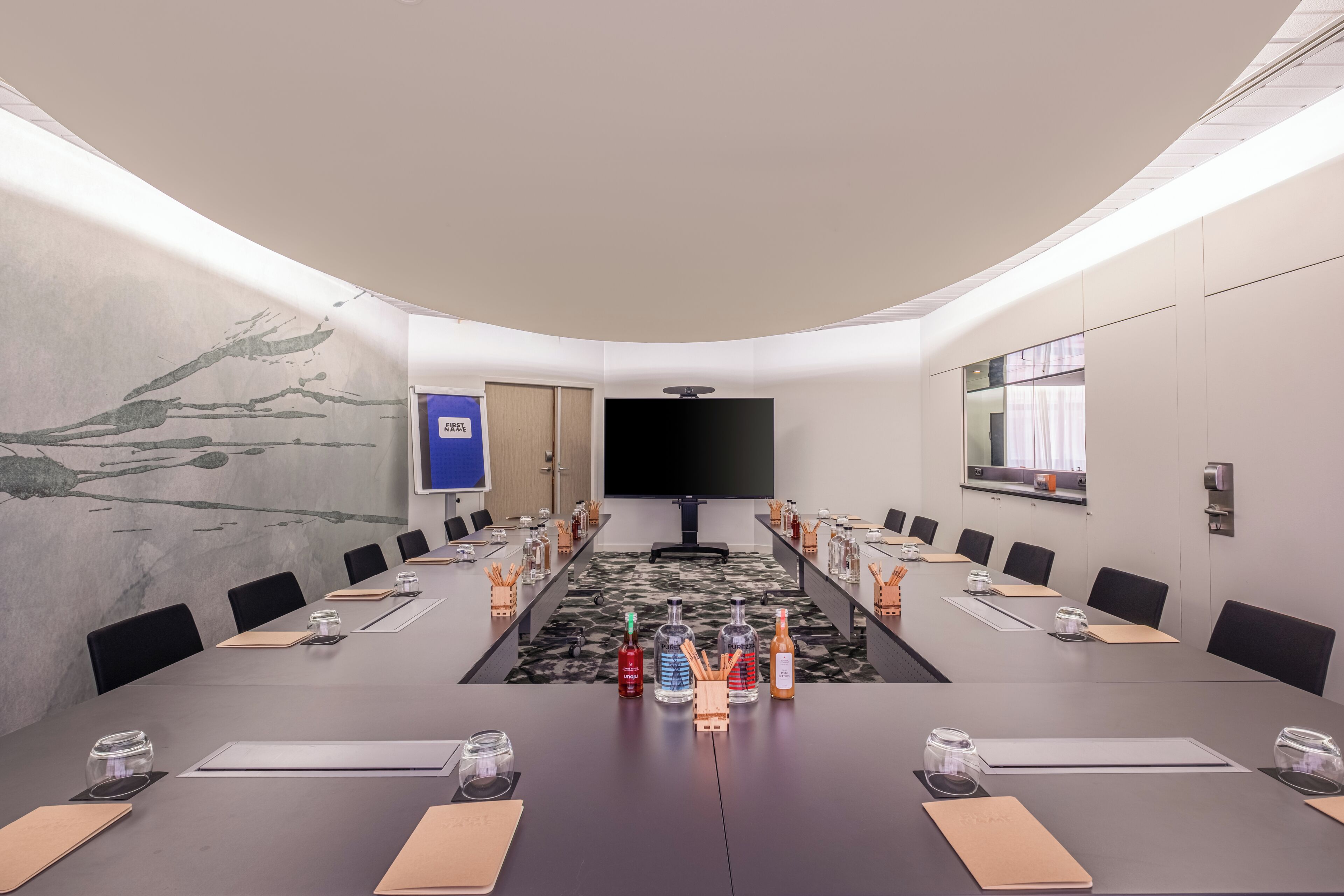 A conference room with a long table, chairs, and a large screen at the front.
