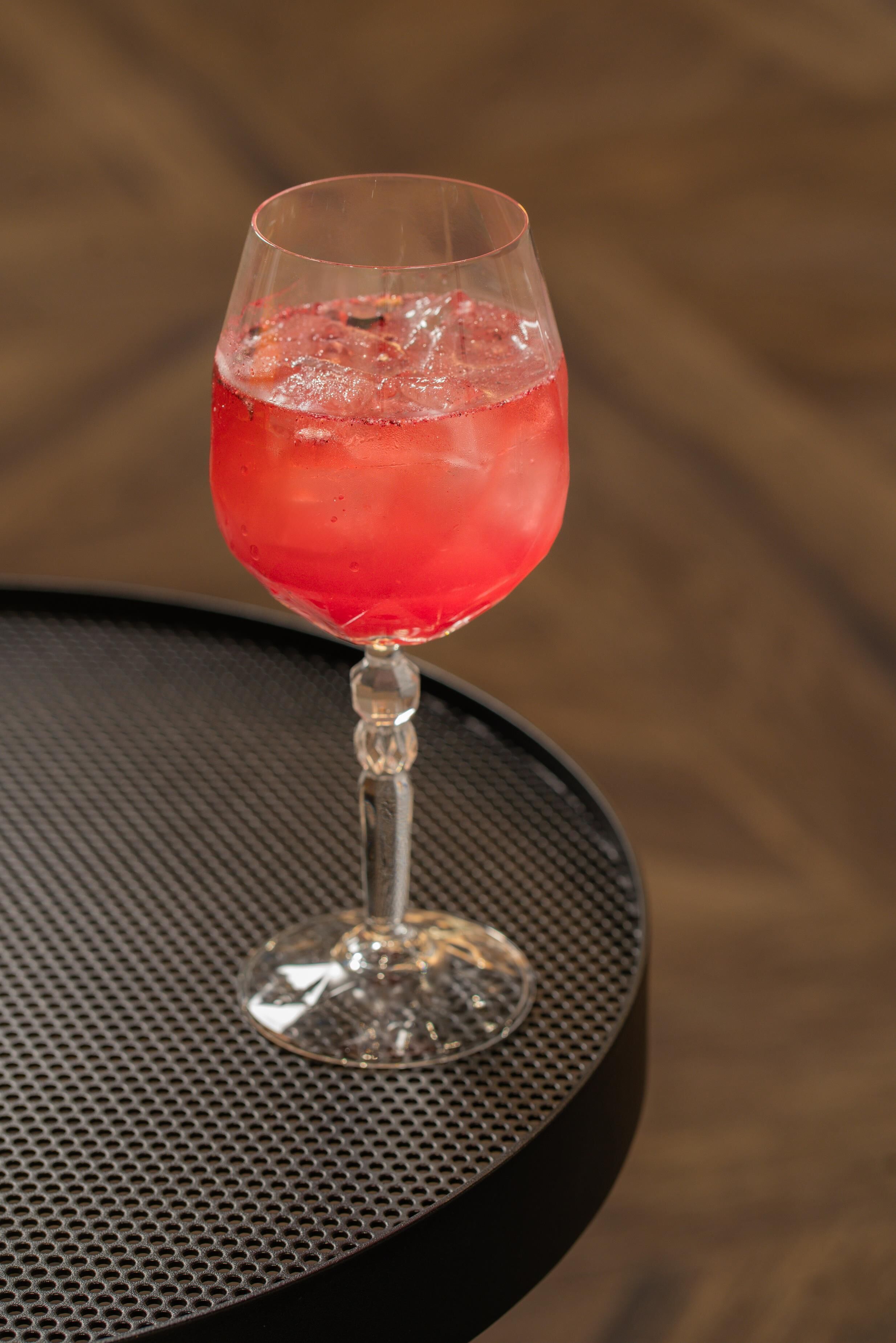 Un verre d’une boisson rouge est posé sur une table ronde dont la surface est percée de trous.