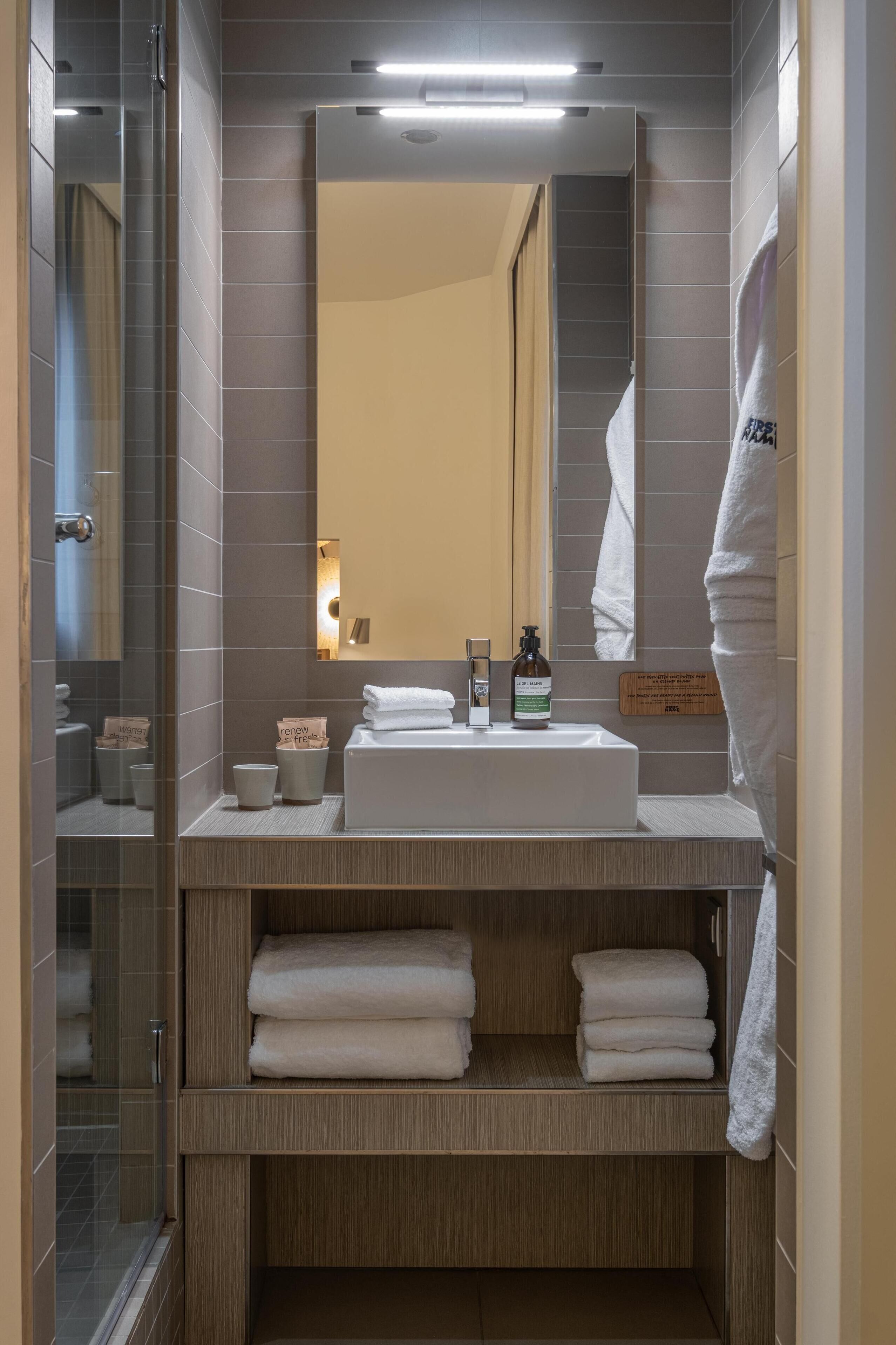A modern bathroom with a glass shower enclosure, a large mirror, a white sink, and neatly folded towels.