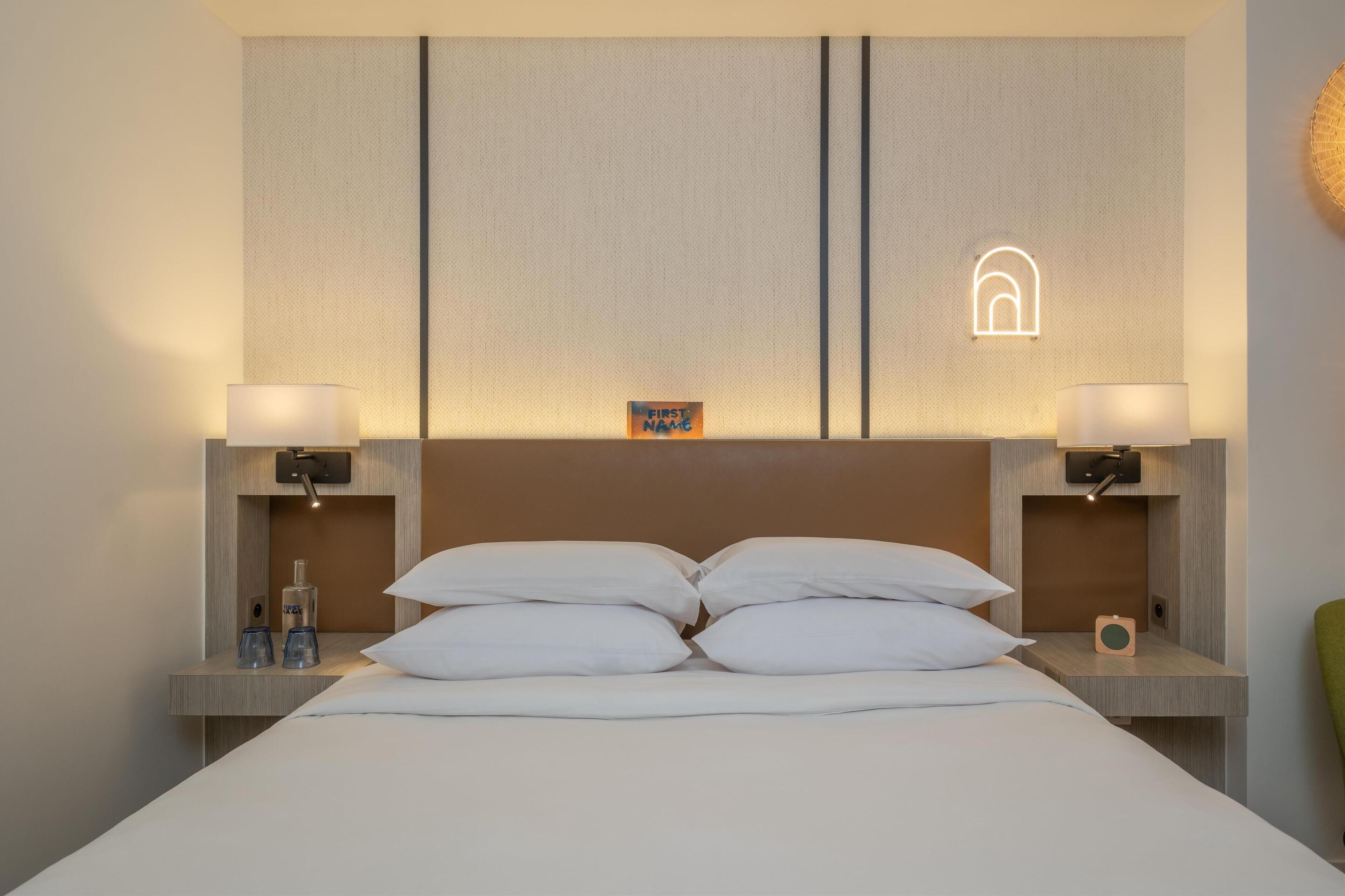 Habitación de hotel con una cama grande, dos mesitas de noche y un cabecero con una lámpara.