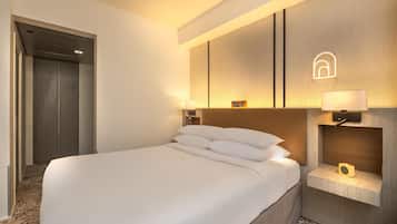 A hotel room with a large bed, a nightstand with a lamp, a wall-mounted shelf, and a door leading to another room.