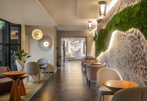Un hall d’hôtel moderne avec un plancher en bois, des espaces de détente et un mur végétal agrémenté d’une cascade.