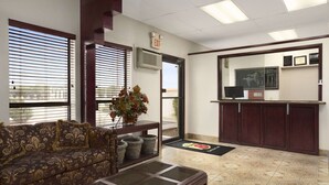 A reception area with a sofa, a coffee table, a potted plant, a reception desk, a television, and a door with an exit sign.
