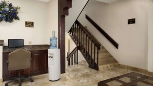 A reception area with a desk, computer, water cooler, and a staircase.