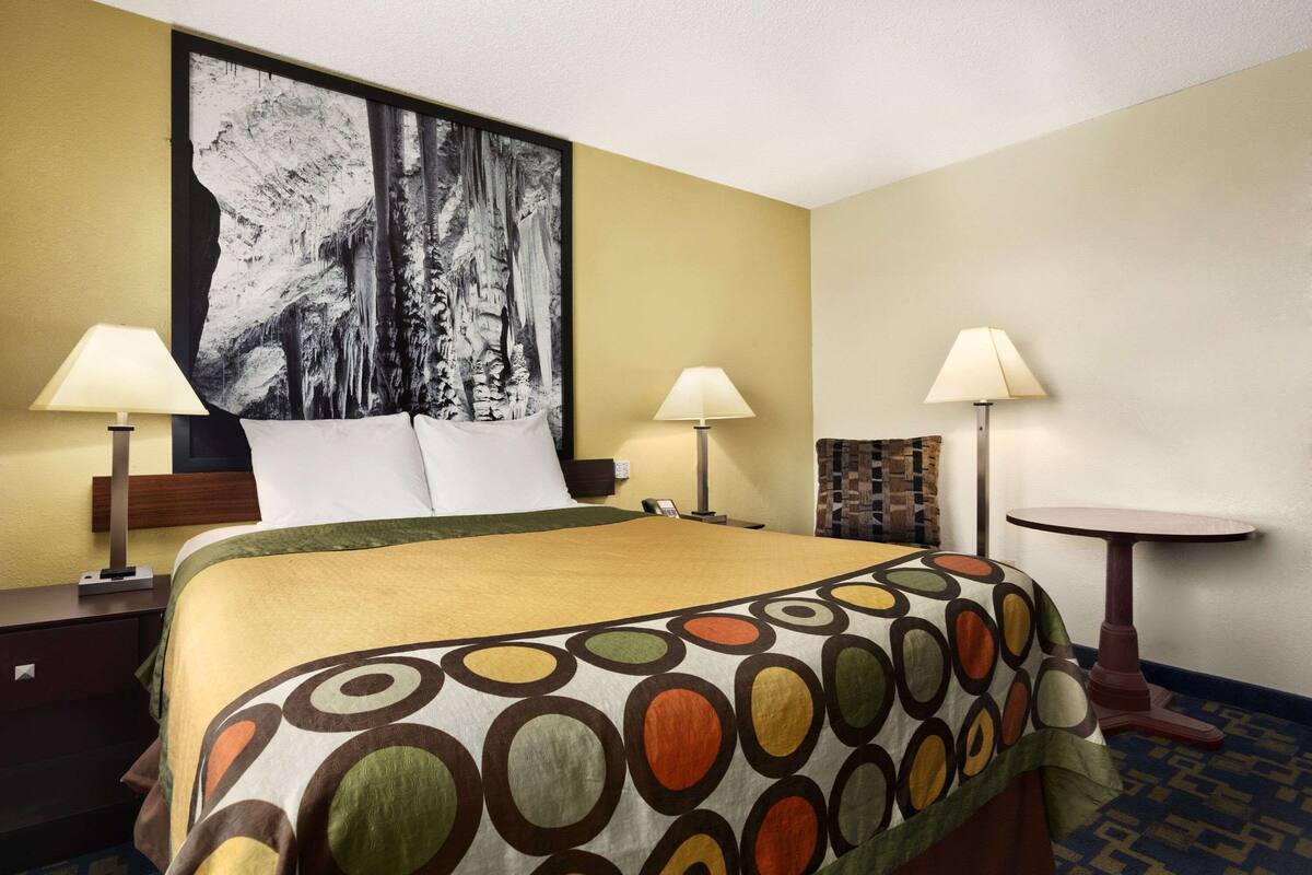 A hotel room with a large bed, two bedside tables with lamps, a small round table, and a large abstract painting on the wall.