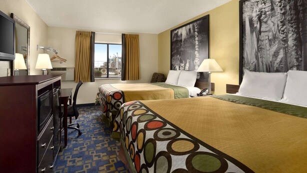 A hotel room with two beds, a desk, a chair, a TV, and a window with curtains.
