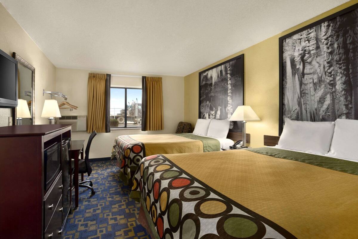 A hotel room with two beds, a desk, a chair, a TV, and a window with curtains.