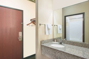 A bathroom with a wooden door, a granite countertop sink, a mirror, and a towel rack with white towels.