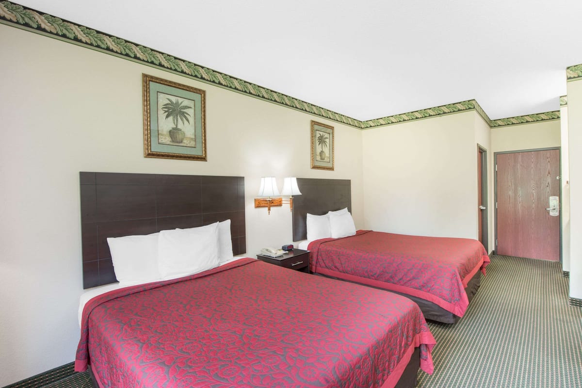 Ein Hotelzimmer mit zwei Betten, jeweils mit roter Bettdecke, einem Nachttisch mit Lampe und einem gerahmten Bild an der Wand.