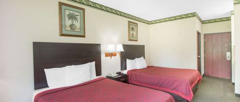 Une chambre d’hôtel avec deux lits, chacun recouvert d’une couverture rouge, une table de chevet avec une lampe et un tableau encadré au mur.