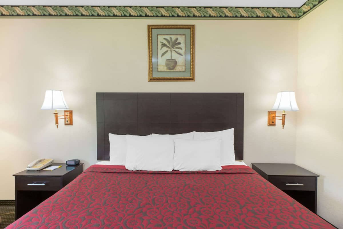 Ein Hotelzimmer mit einem großen Bett, zwei Nachttischen, einer Ablagefläche und einem gerahmten Bild an der Wand, sowie zwei Wandleuchten.