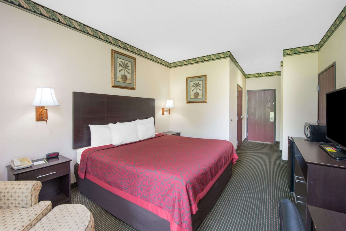Ein Hotelzimmer mit einem großen Bett, zwei Nachttischen, einem Schreibtisch mit Fernseher, einem Sessel und einer Tür zu einem weiteren Raum.