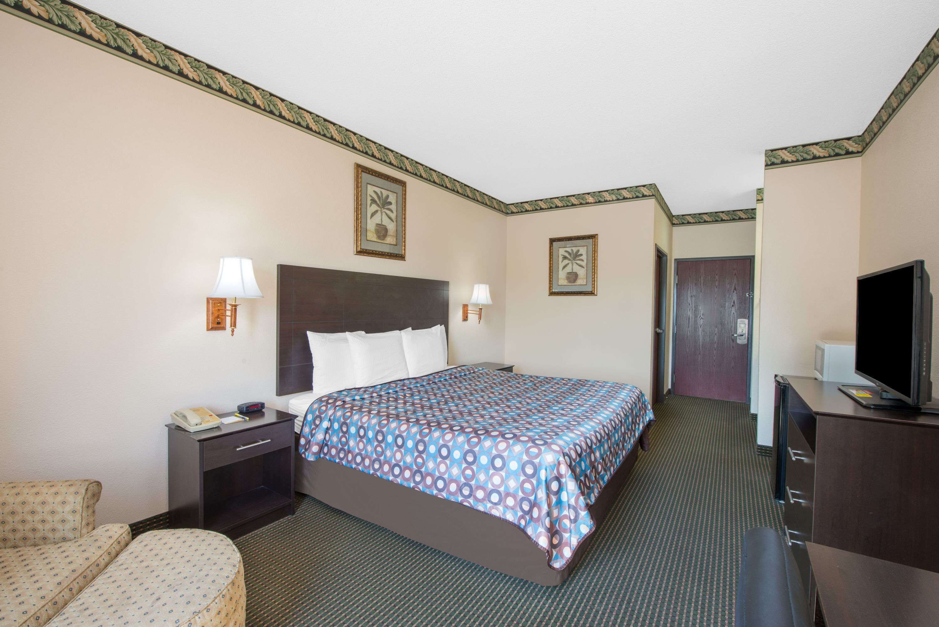 A hotel room with a bed, bedside tables, a desk, a chair, a television, and framed pictures on the walls.