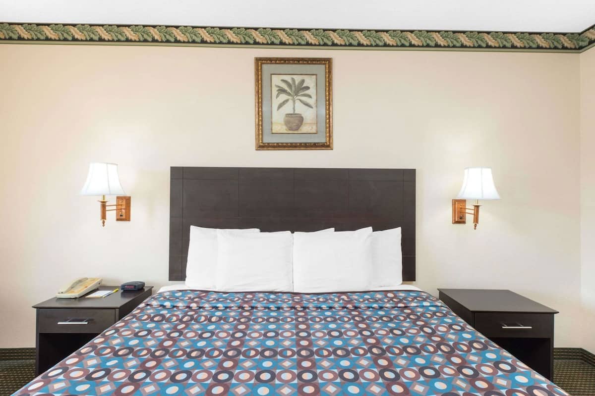 Ein Hotelzimmer mit einem großen Bett, zwei Nachttischen, einer Ablage und einem gerahmten Bild an der Wand, sowie zwei Wandleuchten.