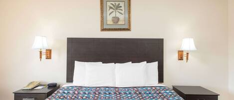 A hotel room with a large bed, two bedside tables, a nightstand, a framed picture on the wall, and two wall-mounted lamps.