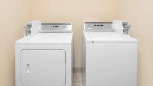 Two white front-loading washing machines in a laundry room with beige walls and a tiled floor.