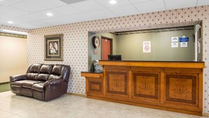 A reception area with a leather sofa, a wooden reception desk, and a wall with patterned wallpaper and a framed picture.
