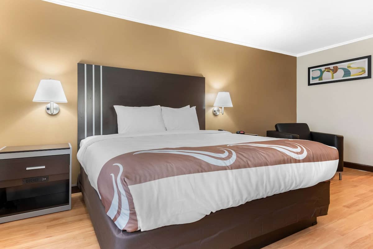 A hotel room with a large bed, two bedside lamps, a nightstand, a chair, and a framed picture on the wall.