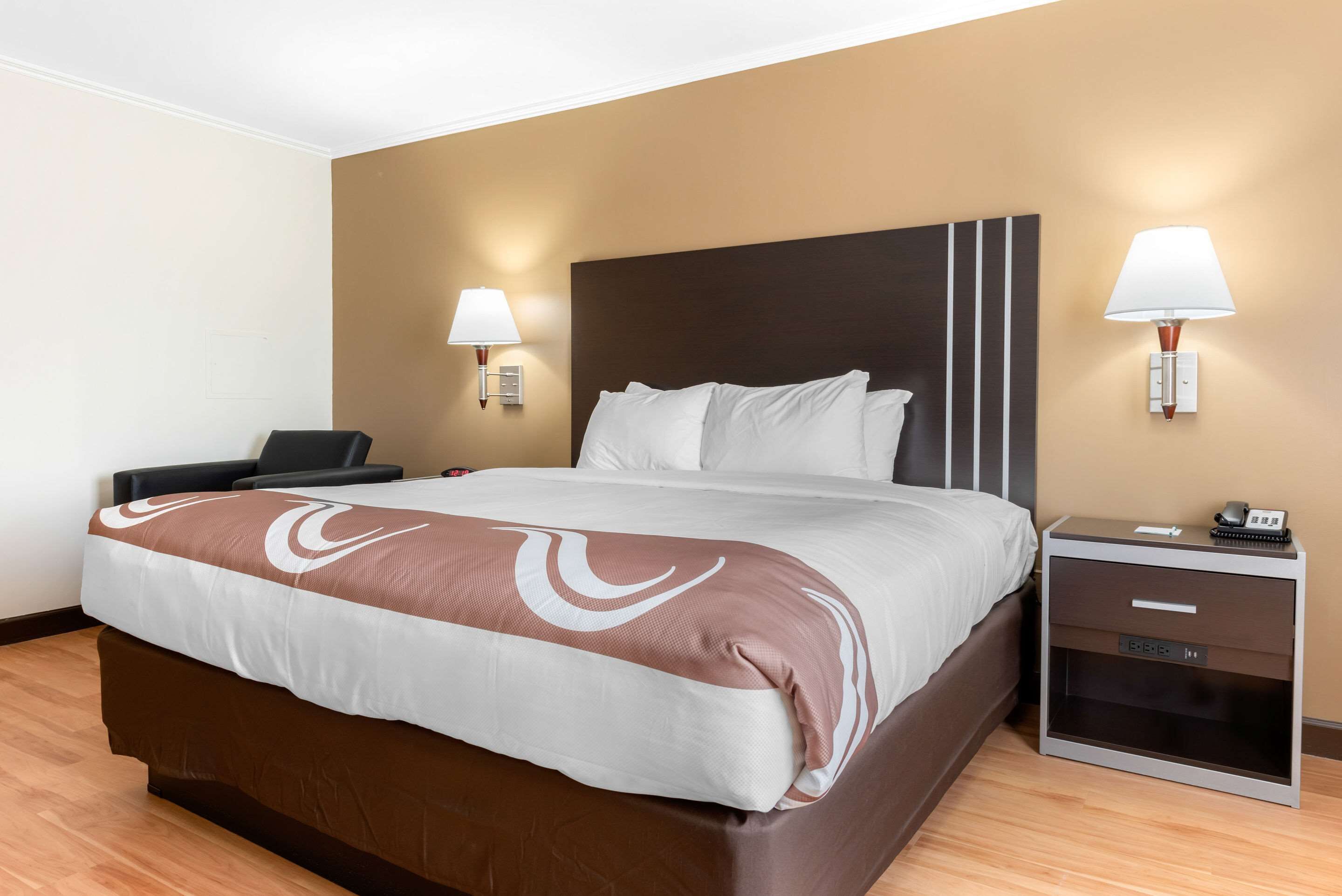 A hotel room with a large bed, bedside tables, and wall-mounted lamps.